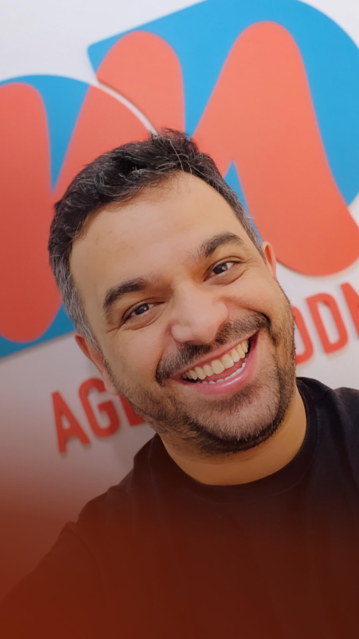 Douglas Oliveira sorrindo em frente ao logo da Agência DDM